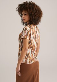Short-sleeve t-shirt in soft fabric featuring a brown, cream, and orange abstract pattern; crew neckline and relaxed fit.