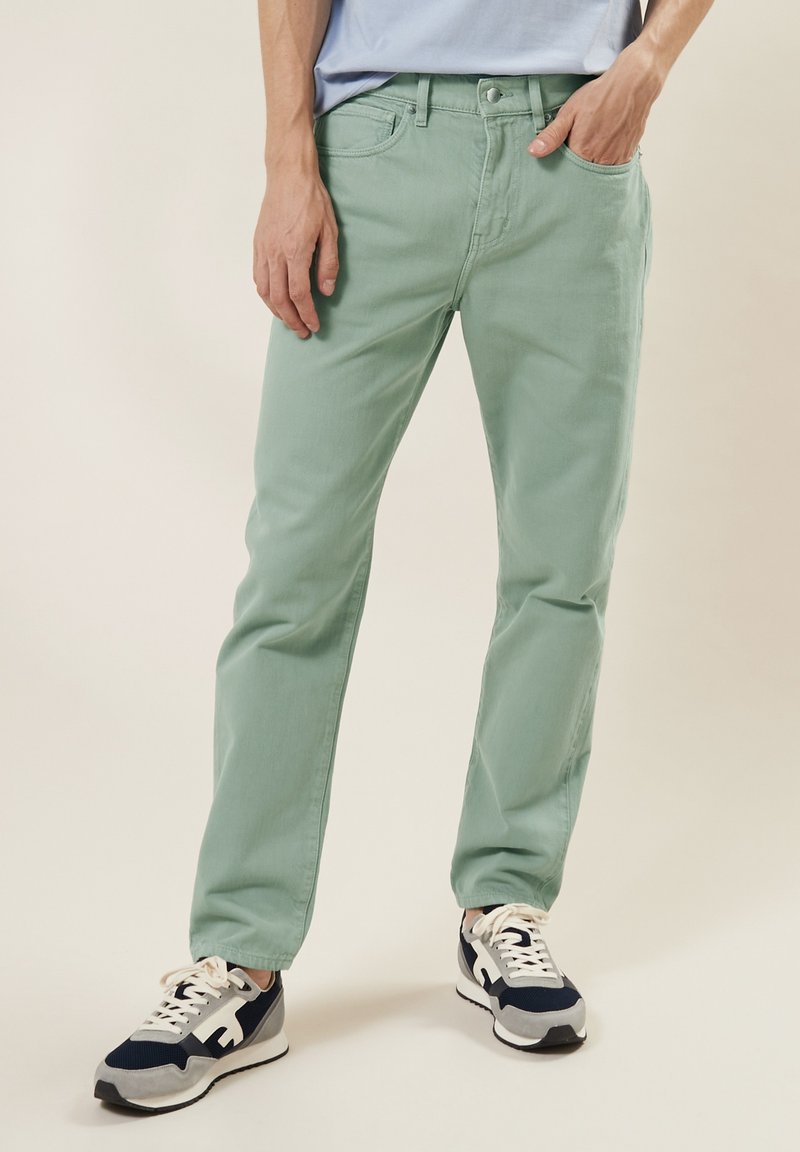 Lichtgroene katoenen broek met een recht model, vijf zakken en een ritssluiting. Draag het met marineblauwe en grijze sneakers met witte accenten.