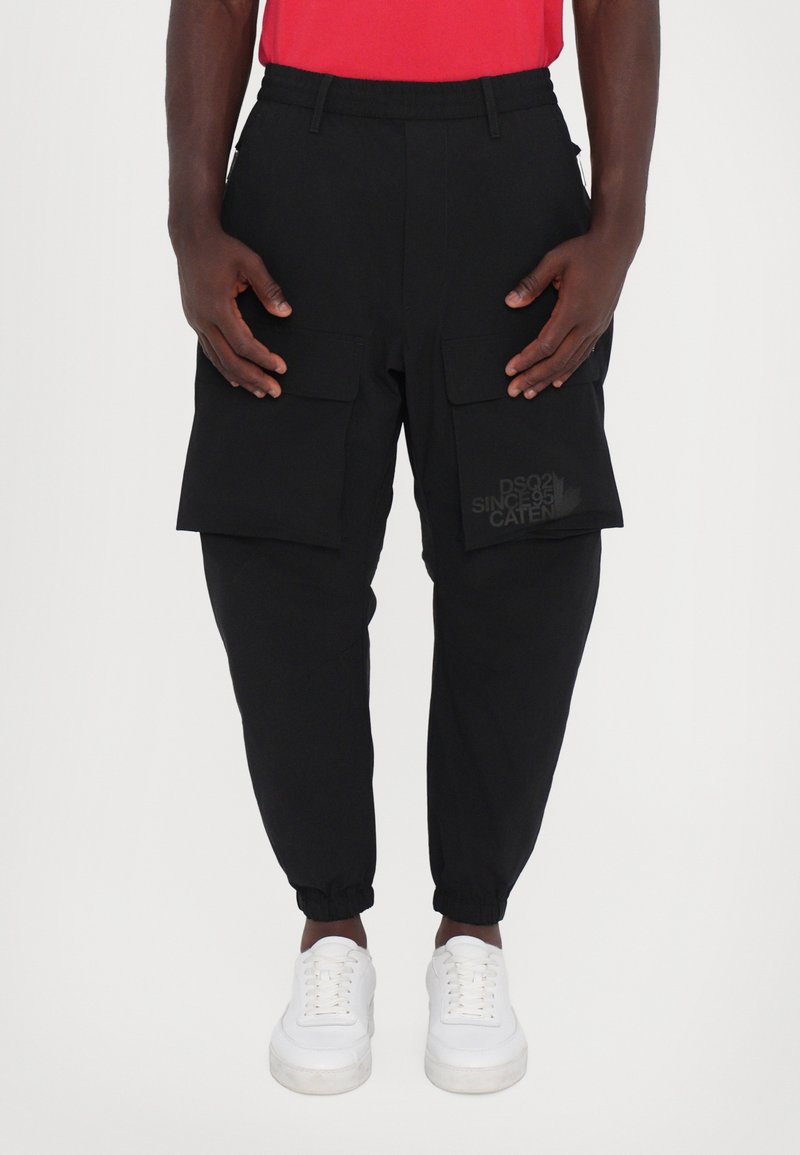 Black cargo pants with an elastic waistband, cuffed ankles, two front pockets, and a logo print on the thigh. Paired with white sneakers.