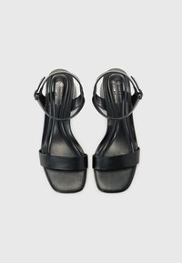 Sandali con tacco in pelle vegana nera, caratterizzati da un design minimalista, con una larga fascia frontale e una fascia per caviglia regolabile.
