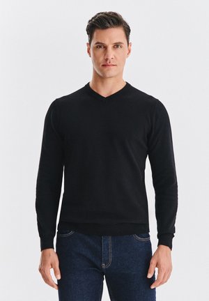 Czarny sweter z długim rękawem i dekoltem w serek, wykonany z miękkiego materiału o gładkiej fakturze. Dopasowany krój z prążkowanymi mankietami i obszyciem, zestawiony z niebieskimi dżinsami.