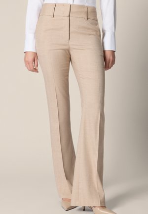 Beżowe, dopasowane spodnie z wysokim stanem z subtelnym wzorem jodełki, noszone z białą koszulą i beżowymi szpilkami z ostrym noskiem.