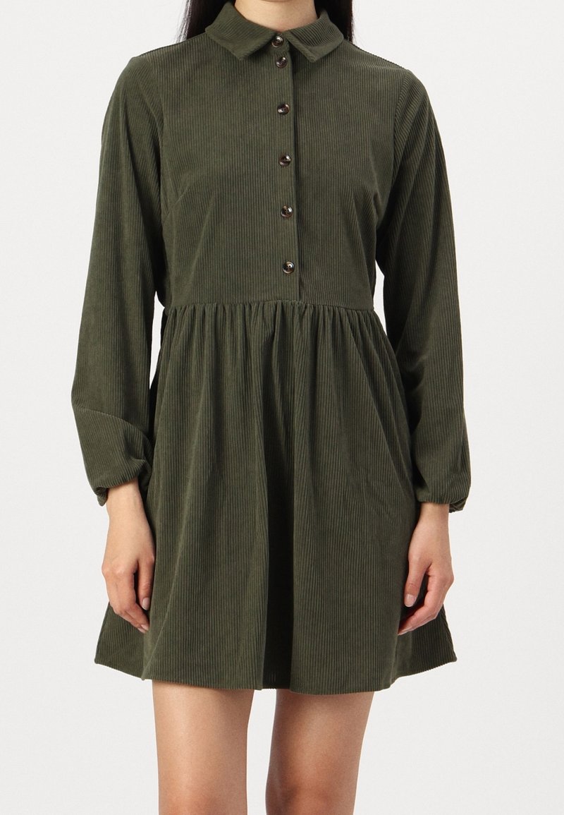 Robe en velours côtelé vert olive à manches longues, avec boutons devant, col, taille froncée et jupe courte évasée.