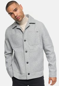 Veste en mélange de laine grise avec un col, deux poches avant et des boutons noirs. Dispose d'une texture lisse et d'un design à coupe décontractée.