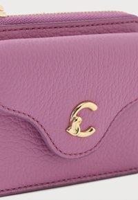 Purple leather wallet with a textured finish, featuring a gold logo accent, and a gold zipper. Stitched edges contrast the material.