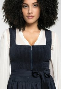 Navy blauwe corduroy jurk met een aansluitend lijfje, ritssluiting en een satijnen strik in de taille. Heeft een kant afgewerkt kraag en een vloeiende rok.