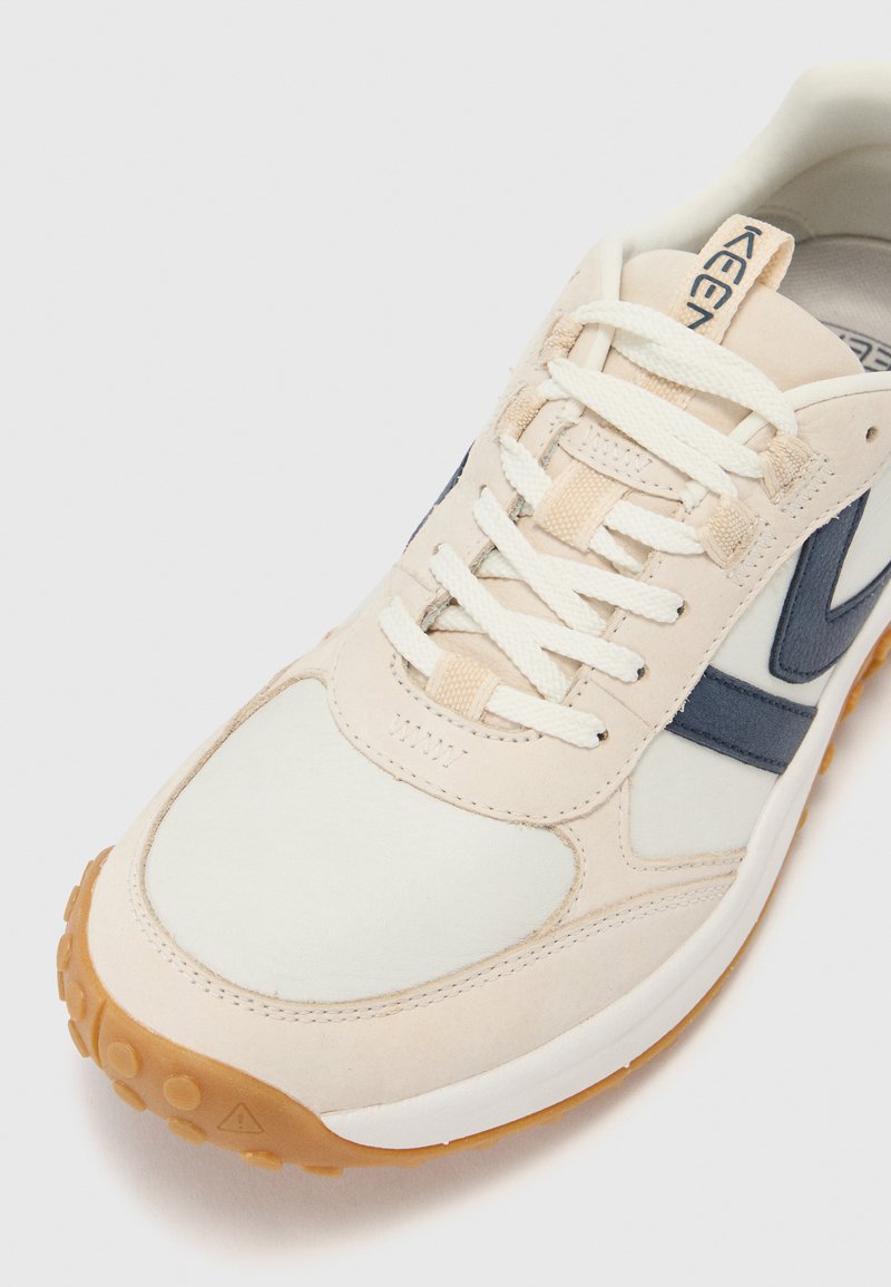 Beige undmarinefarbene Sportschuh mit einem glatten synthetischen Obermaterial, Schnürverschluss, gepolstertem Kragen und strukturiertem Gummisohle.