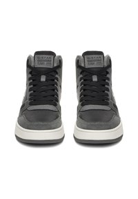 Mustat ja hallid kõrge profiiliga tossud, millel on segu nahast ja sametist tekstuuridest, mustad nöörid ning valge kummist tallaosa logodetailidega.