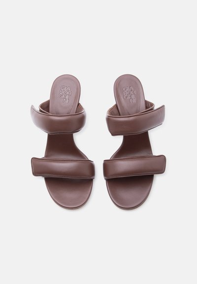 Καφέ δερμάτινα σανδάλια χωρίς λουράκια με δύο φαρδιές επενδεδυμένες λουρίδες και επίπεδες σόλες, με το όνομα της μάρκας χαραγμένο στις εσωτερικές σόλες.