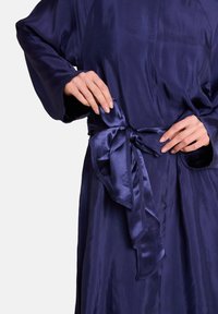 Marineblå satinrobe med lange ærmer, som har et bundet belte i livet og en glatt tekstur. Stoffet har en subtil glans og faller elegant.