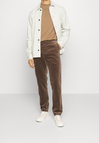 Chemise à rayures gris clair avec boutons, t-shirt côtelé marron, pantalon en velours côtelé marron et baskets blanches avec œillets multicolores.