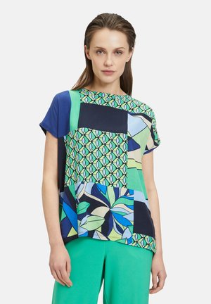 Kurzarmbluse mit einem Patchwork-Design in blauen, grünen und schwarzen Mustern. Aus leichtem Stoff gefertigt; lockere Passform.