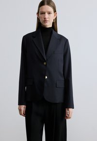 Marineblauwe blazer met een getailleerde pasvorm, een enkelrijig ontwerp, gouden knopen, twee voorzakken en een minimalistische stijl. Gemaakt van gladde stof.