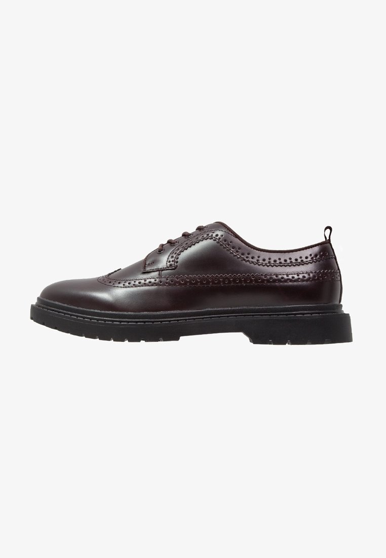 Chaussure brogue en cuir marron foncé avec un design à bout ailé, détails perforés, fermeture à lacets et semelle épaisse en caoutchouc noir.