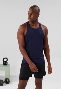 Marinblå ärmlös linne i mjukt tyg med en diskret logotyp. Matchas med svarta sportshorts.