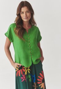 Blusa di lino verde con scollo rotondo e maniche corte arrotolate, dotata di una fila di bottoni in legno lungo la parte anteriore.