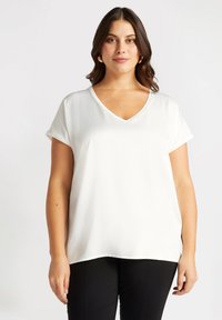 Top blanco de manga corta con escote en V, tejido suave, corte relajado y dobladillo redondeado. Sin patrones ni acentos visibles.