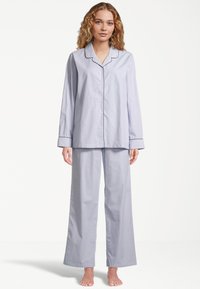 Vaatekokonaisuus sisältää vaaleansiniraidalliset puuvillapijamasetit, joissa on napitettava pitkähihaine paita ja leveälahkeiset housut, joissa on kaulus ja mustat reunukset.