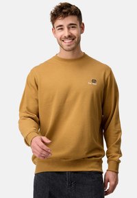 Sennepsgul sweatshirt med lange ærmer og ribbede manchetter, prydet med et lille broderet logo på brystet. Blød, tekstureret stof.
