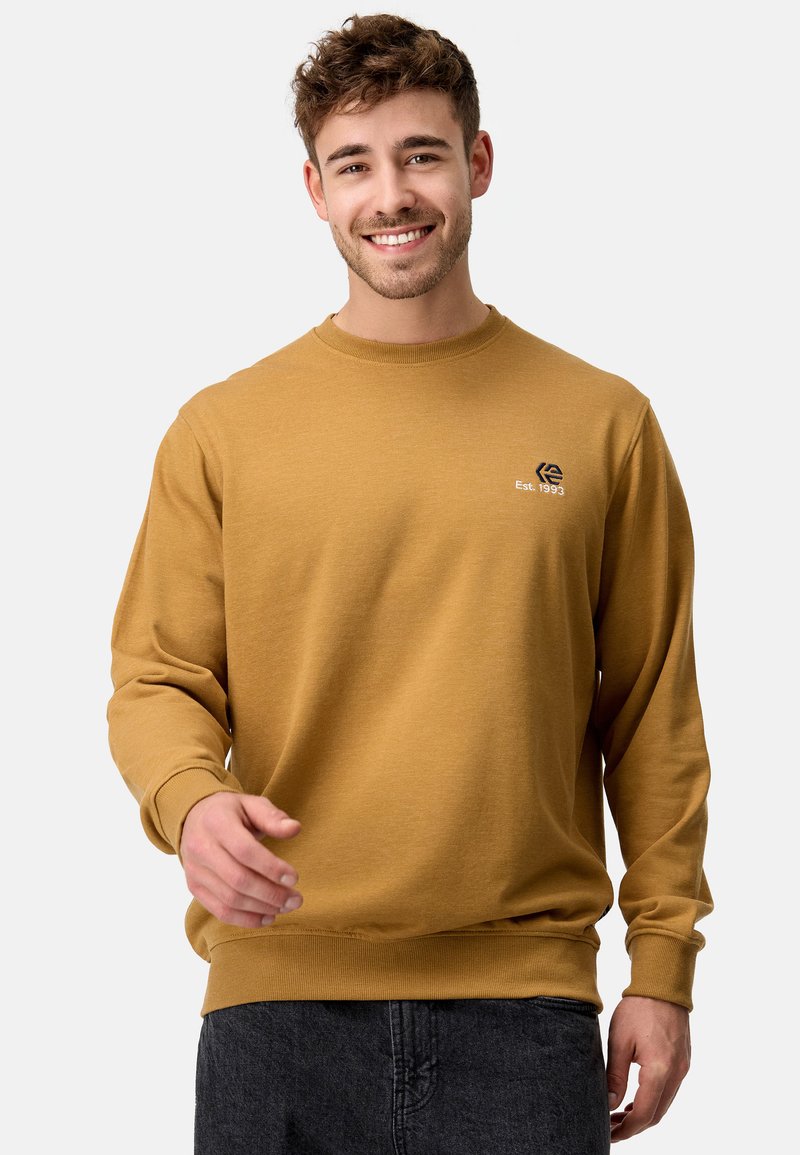 Sennepsgul sweatshirt med lange ærmer og ribbede manchetter, prydet med et lille broderet logo på brystet. Blød, tekstureret stof.