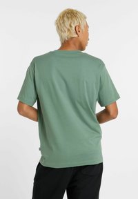 Grøn kortærmet t-shirt lavet af blødt stof; afslappet pasform med en klassisk rund hals; har et lille logo tag ved kanten.