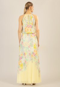 Blumen-gefaltetes Maxikleid in einem hellen Gelbton. Weicher, transparenter Stoff mit pastellfarbenen Blumenmustern, Halterneck-Design mit Knopfdetails.