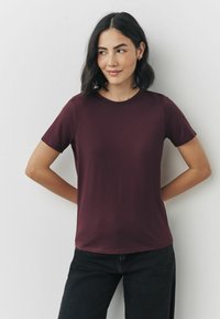 Bordeaux kortærmet t-shirt med rund halsudskæring, glat tekstur og slim fit, parret med sorte bukser. Ingen synlige mønstre eller accenter.