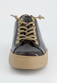 Zwarte lakleren sneaker met gouden oogjes, beige veters en een gestructureerde beige rubberen zool. Ronde neus en gladde afwerking.