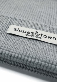 Szara dziana czapka z prążkowanym wzorem, z białą metką, na której widnieje napis "slopes&town AMSTERDAM."
