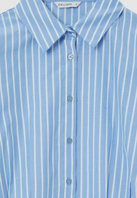 Chemise bleu clair à boutons avec des rayures blanches verticales, dotée d'un col classique et de boutons bleus, fabriquée dans un tissu lisse.