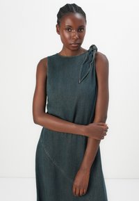 Denim dress in dark blue with a sleeveless design and a knotted shoulder detail. Features a diagonal seam and smooth texture.
