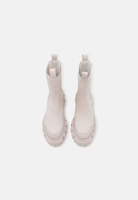 Paire de bottines à semelle épaisse de couleur crème avec languettes de traction, vue de dessus sur un fond blanc.