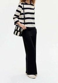 Top de manga larga a rayas blancas y negras combinado con pantalones negros de pierna ancha. La modelo sostiene un pequeño bolso de hombro a rayas.