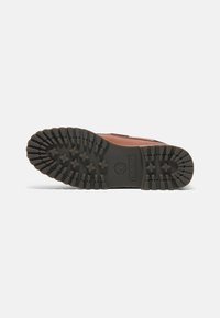 Chaussure en cuir brun avec une semelle extérieure en caoutchouc noir arborant un motif de semelle en étoiles et en crêtes, comprenant un logo Timberland en relief.