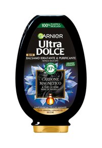 Bottiglia di plastica nera Garnier Ultra Dolce con accenti dorati. Presenta un design floreale blu e un'etichetta che evidenzia gli ingredienti di carbone attivo e olio di nigella.
