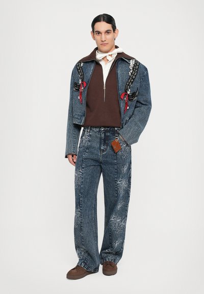 Denim jakk, millel on lilleline tikand ja punased detailid, kombineeritud sobiva mustriga teksadega. All on pruun tõmblukuga kampsun. Pruunad kingad.
