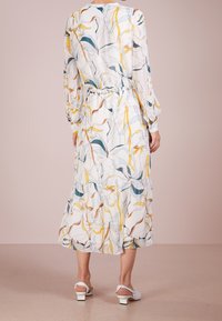 Robe à manches longues avec un imprimé floral en blanc, ornée d'accents jaunes et bleus, dotée d'une taille cintrée et d'un ourlet volé, assortie avec des sandales blanches.