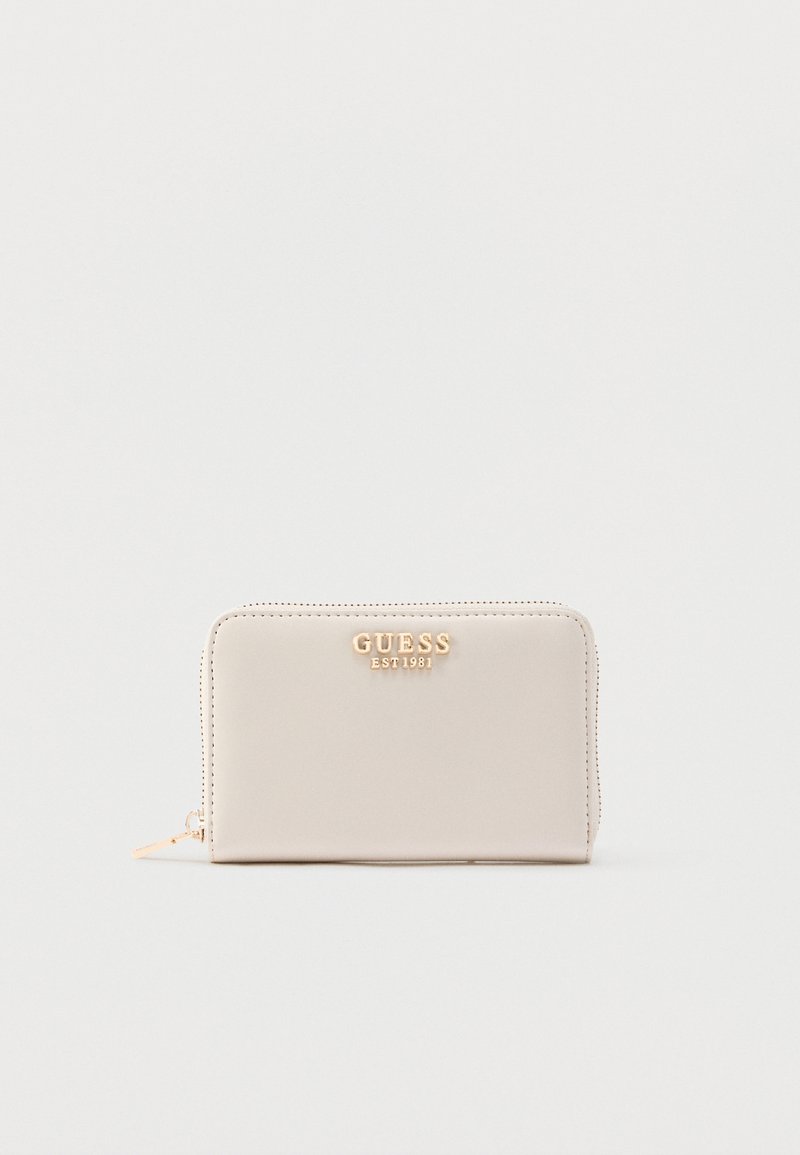Bézs színű cipzáros pénztárca sima anyagból, aranyszínű "GUESS EST 1981" márkajelzéssel és varrott díszítéssel.
