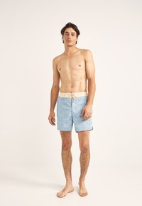 Bañador azul con un diseño texturizado, fabricado con un material ligero, y con una cinturilla elástica con ajuste de cordón, llevado por un modelo.