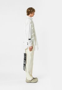 Camisa blanca de botón con tiras verticales, combinada con pantalones crema y zapatos beige texturizados. Presenta etiquetas negras en la ropa.