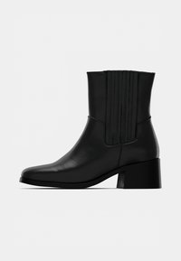 Černá kotníková bota z kůže s špičatou špičkou, svislými švy na svršku a robustním blokovým podpatkem. Hladká textura.