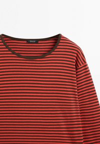 Brązowo-czerwona koszula z długim rękawem w paski, z zaokrąglonym dekoltem i widoczną metką marki wewnątrz kołnierza.