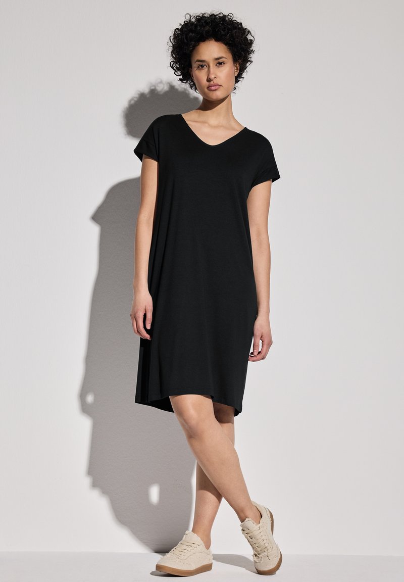 Svart knä-lång klänning med V-ringning och korta ärmar, tillverkad av mjukt tyg. Matchad med beige snörskor. Enkel design.