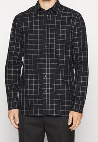 Camicia a maniche lunghe a scacchi bianco e nero con colletto button-down, realizzata in tessuto; presenta una chiusura frontale con bottoni e maniche lunghe.