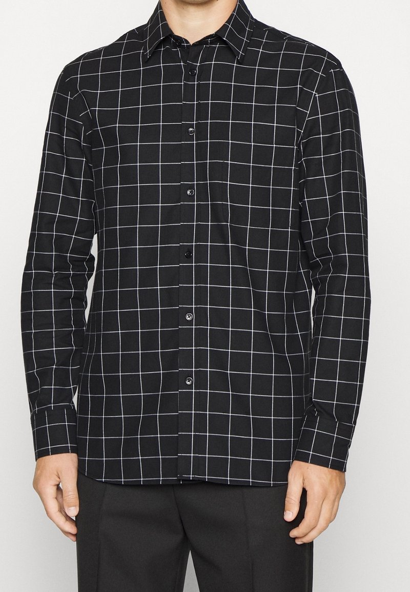 Camicia a maniche lunghe a scacchi bianco e nero con colletto button-down, realizzata in tessuto; presenta una chiusura frontale con bottoni e maniche lunghe.
