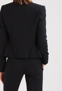 Svart skräddarsydd kavaj med strukturerad passform, utrustad med notchad krage och slät textur, kompletterad med matchande svarta byxor.