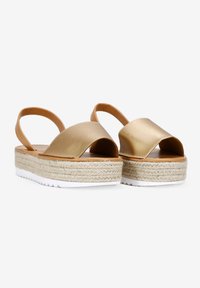 Sandalias de plataforma mate doradas con tiras cruzadas, plantilla de yute trenzado y suela de goma blanca. Textura suave y diseño casual.