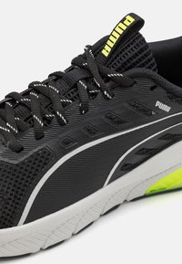 Crne atletske cipele s mrežastim gornjim dijelom i bijelim naglascima. Imaju istaknuti Puma logotip, teksturirane uzorke i svijetlozeleni dio potplata.