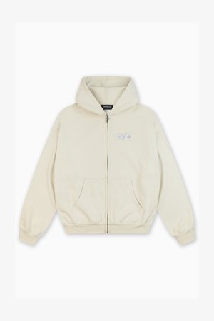 Švarkelis su užtrauktuku šviesiai bežinės spalvos audinyje, su švelnia tekstūra, su mėlynu logotipu priekyje, dviem šoniniais kišenėmis ir su raišteliu ant gobtuvo.