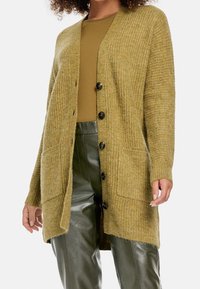 Olivově zelený pletený svetr s výstřihem do V, předními knoflíky a dvěma kapsami. Dlouhé rukávy s ribovanými manžetami. Texturovaná, měkká látka.